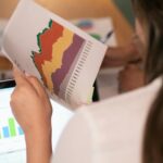 Moderniame biure dirbantys specialistai analizuojantys skaitmeninės rinkodaros rezultatus ekrane.